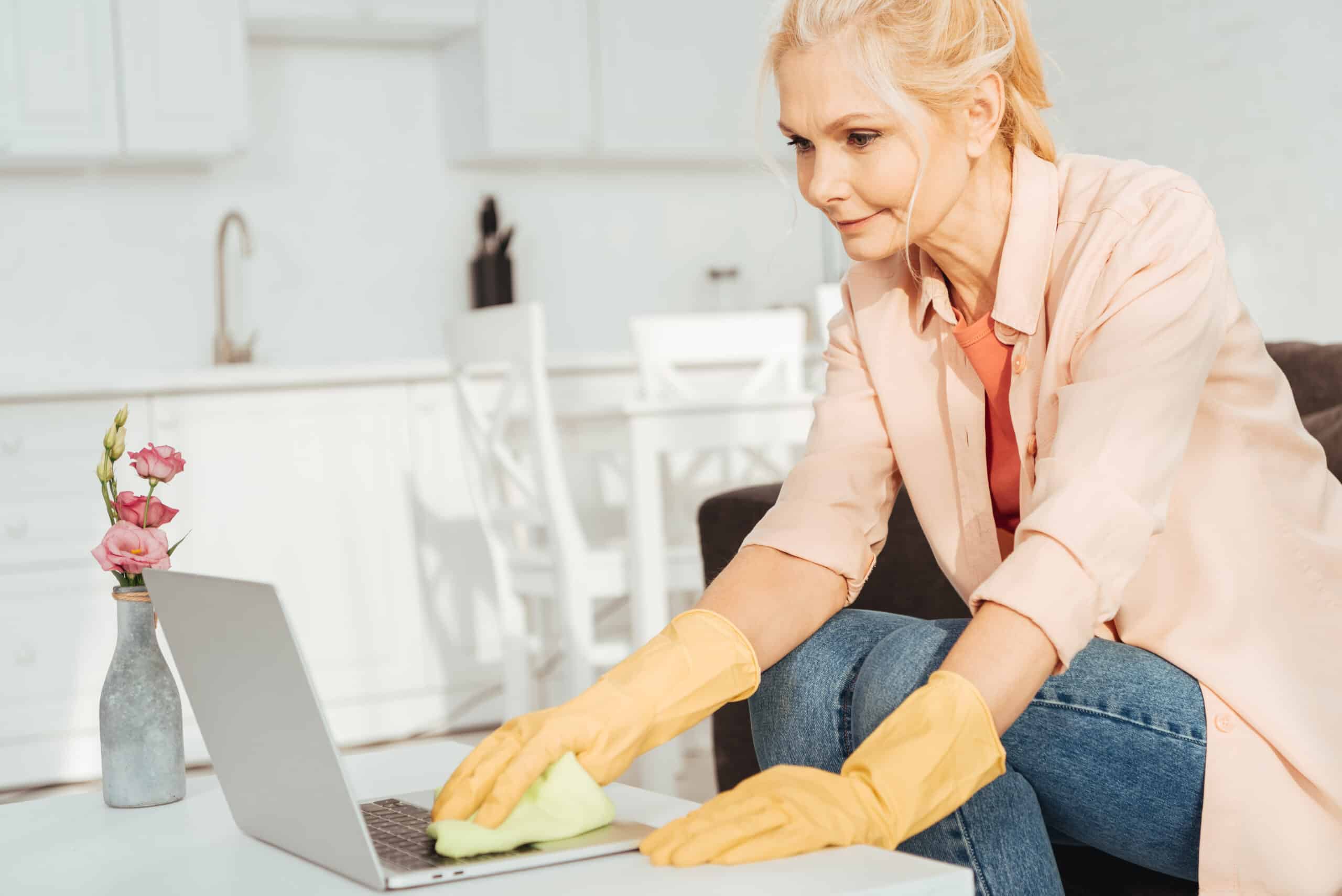 Senior woman in rubber gloves cleaning laptop keyboard for office cleaning London